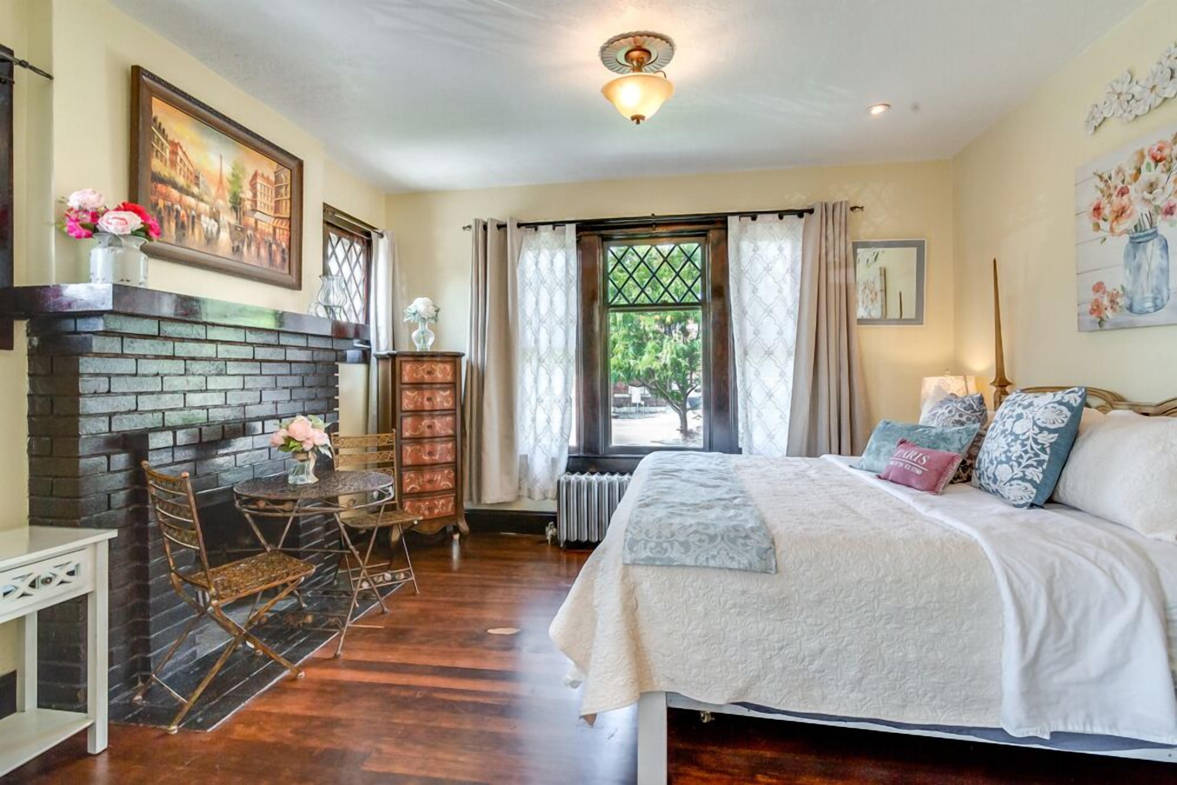 Un dormitorio con chimenea, una cama con almohadas, una ventana con cortinas y un radiador.
