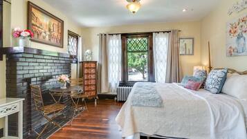 Un dormitorio con chimenea, una cama con almohadas, una ventana con cortinas y un radiador.