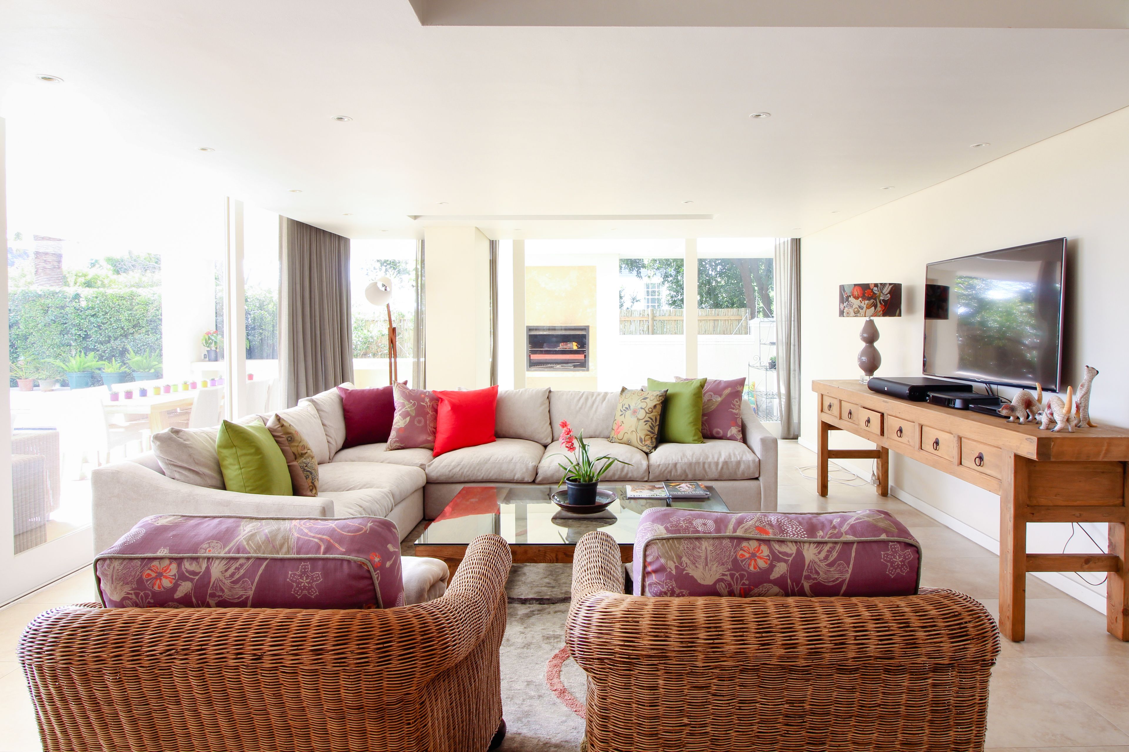 A modern living room with a sofa set, wicker chairs, a coffee table, and a TV on a wooden stand.