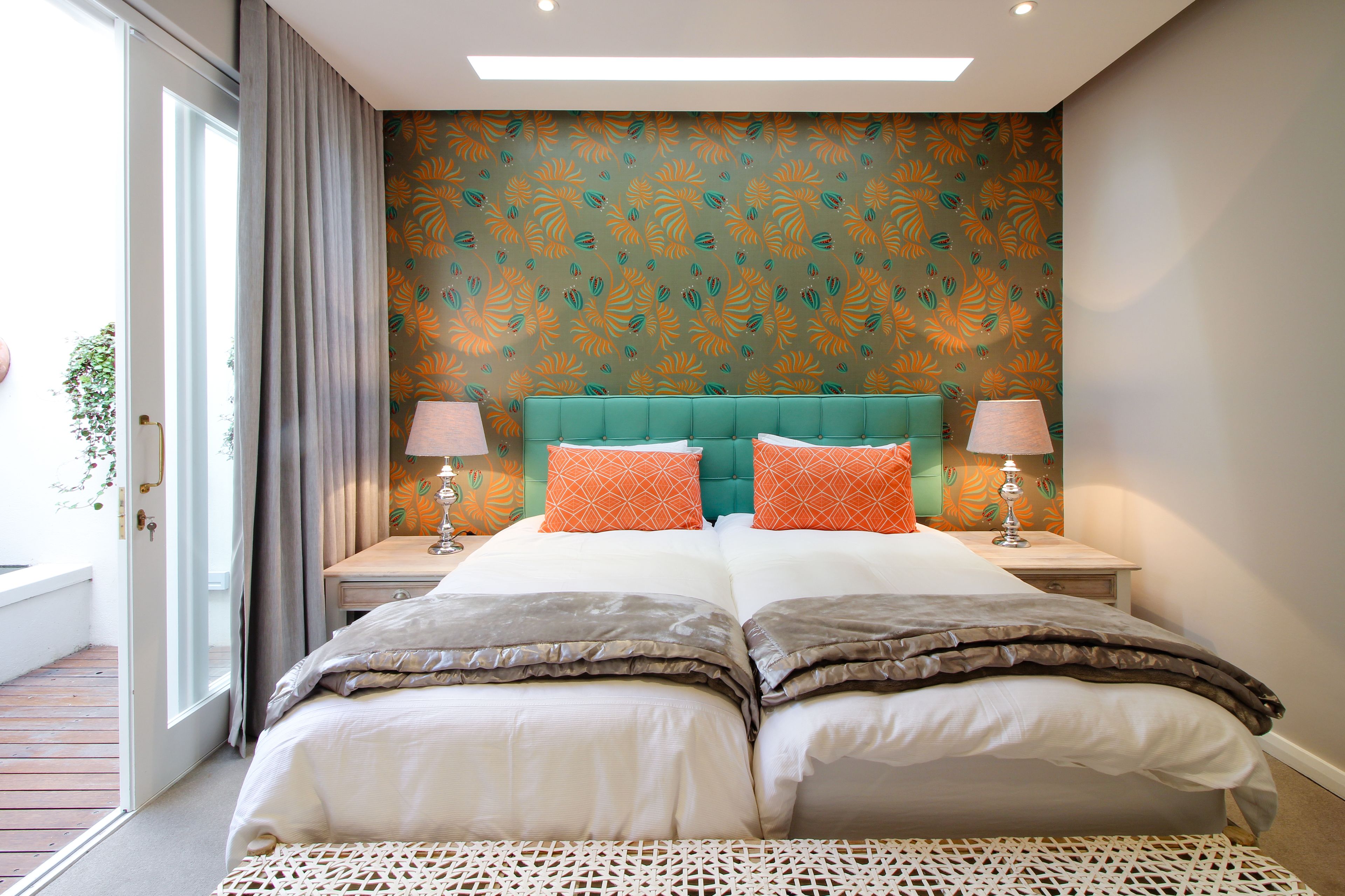 A double bed with two pillows, a teal headboard, and a patterned wall.