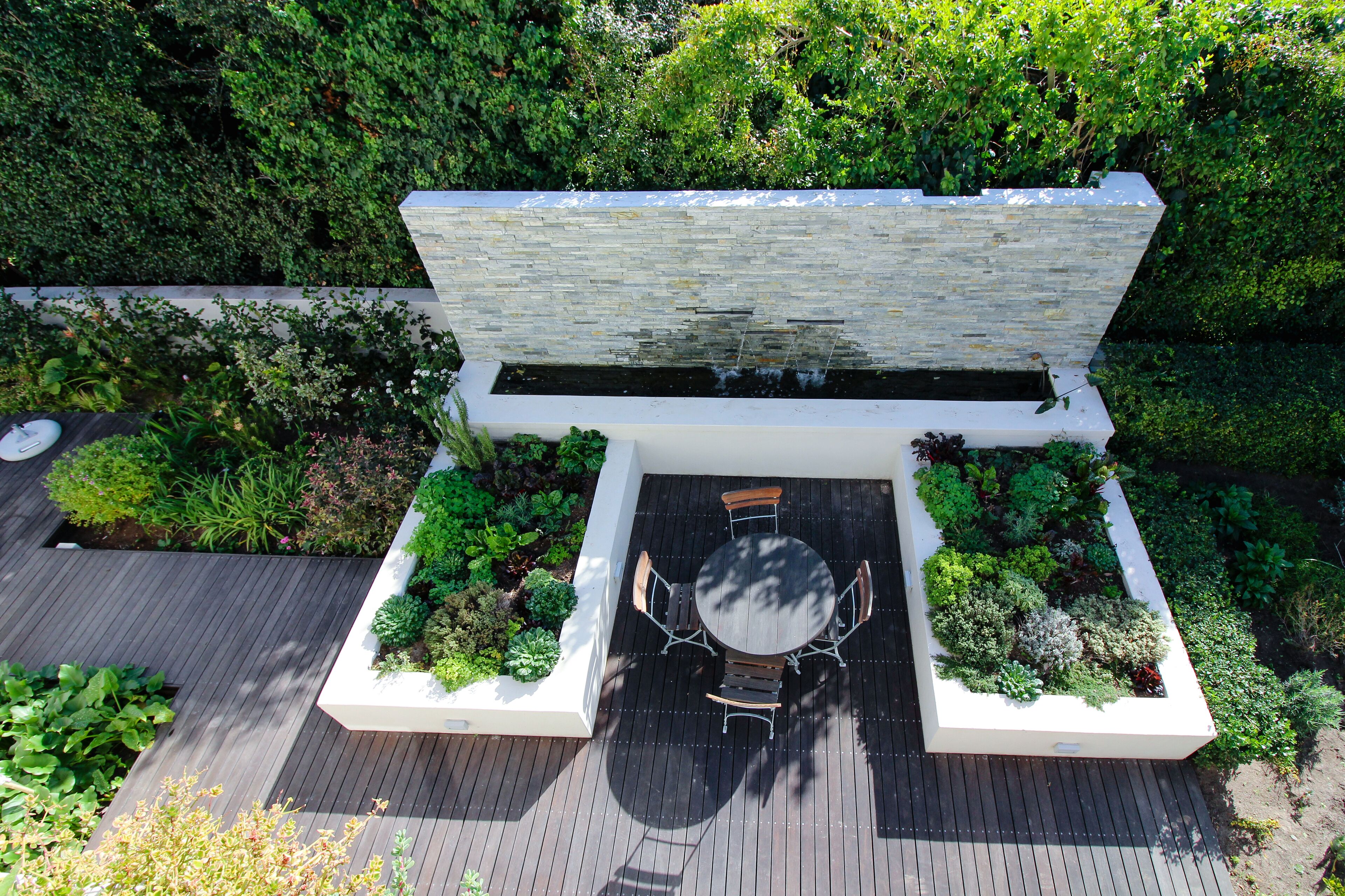 Un giardino pensile con zona pranzo, elemento d'acqua e vegetazione rigogliosa.