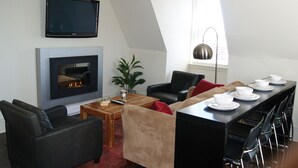 Un salon moderne avec une cheminée, un téléviseur et un coin repas comprenant des chaises et une table.