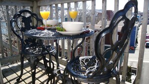 Un balcon avec une table et des chaises, un bol de nourriture et deux verres de jus d’orange.