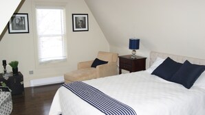 Une chambre avec un grand lit, une chaise, une table de chevet avec une lampe et une fenêtre avec des stores.