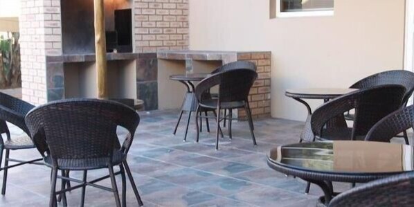 Un patio al aire libre con sillas y mesas de mimbre, una chimenea de ladrillo y un suelo de baldosas.