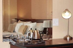 Una habitación de hotel con una cama, una mesita de noche con lámpara, y una bandeja con vasos y tetera.