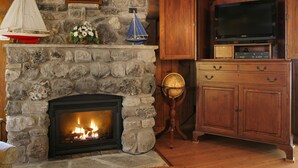 Une cheminée en pierre avec un feu de bois, des meubles en bois, un téléviseur et un globe terrestre.