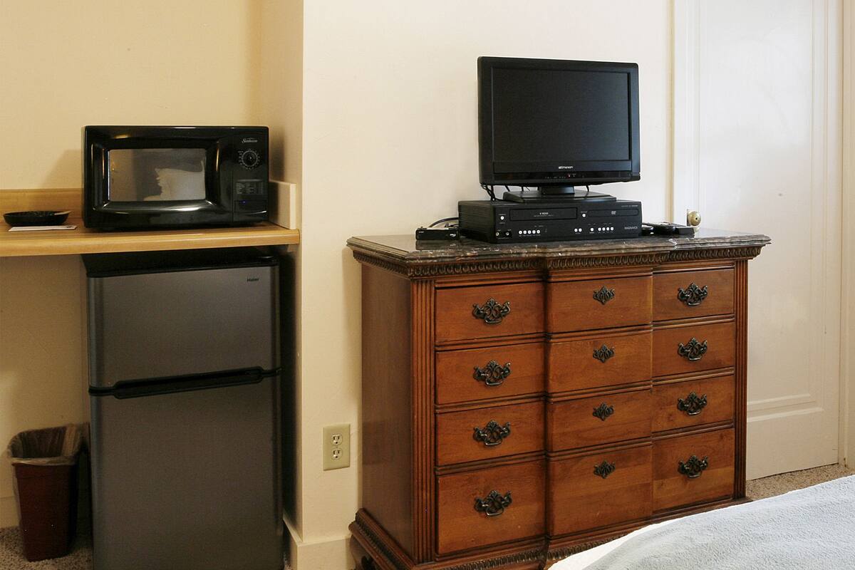 A compact kitchenette with a microwave, refrigerator, and a flat-screen TV on a wooden dresser.