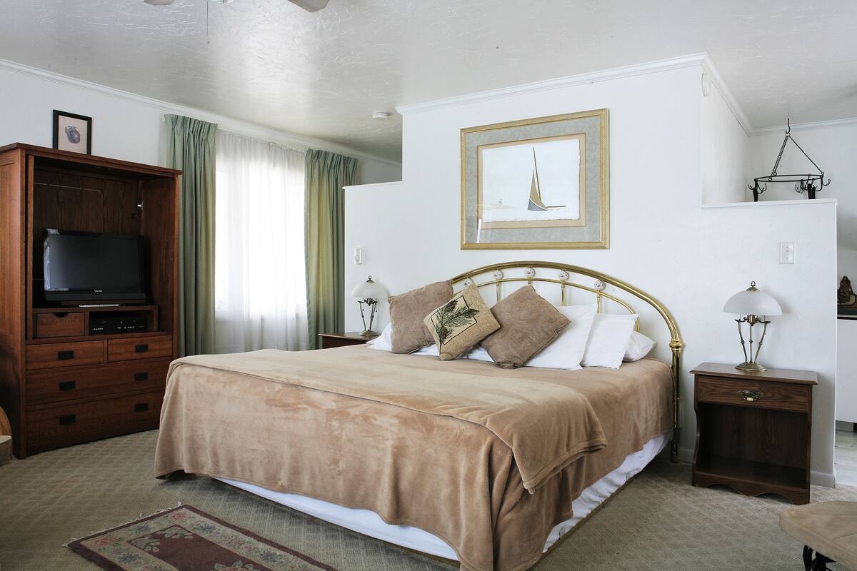 A neatly arranged bedroom with a bed, a wooden dresser, a television, and a framed picture on the wall.
