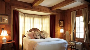Une pièce en bois avec un lit, une chaise, une lampe et une fenêtre avec des rideaux.