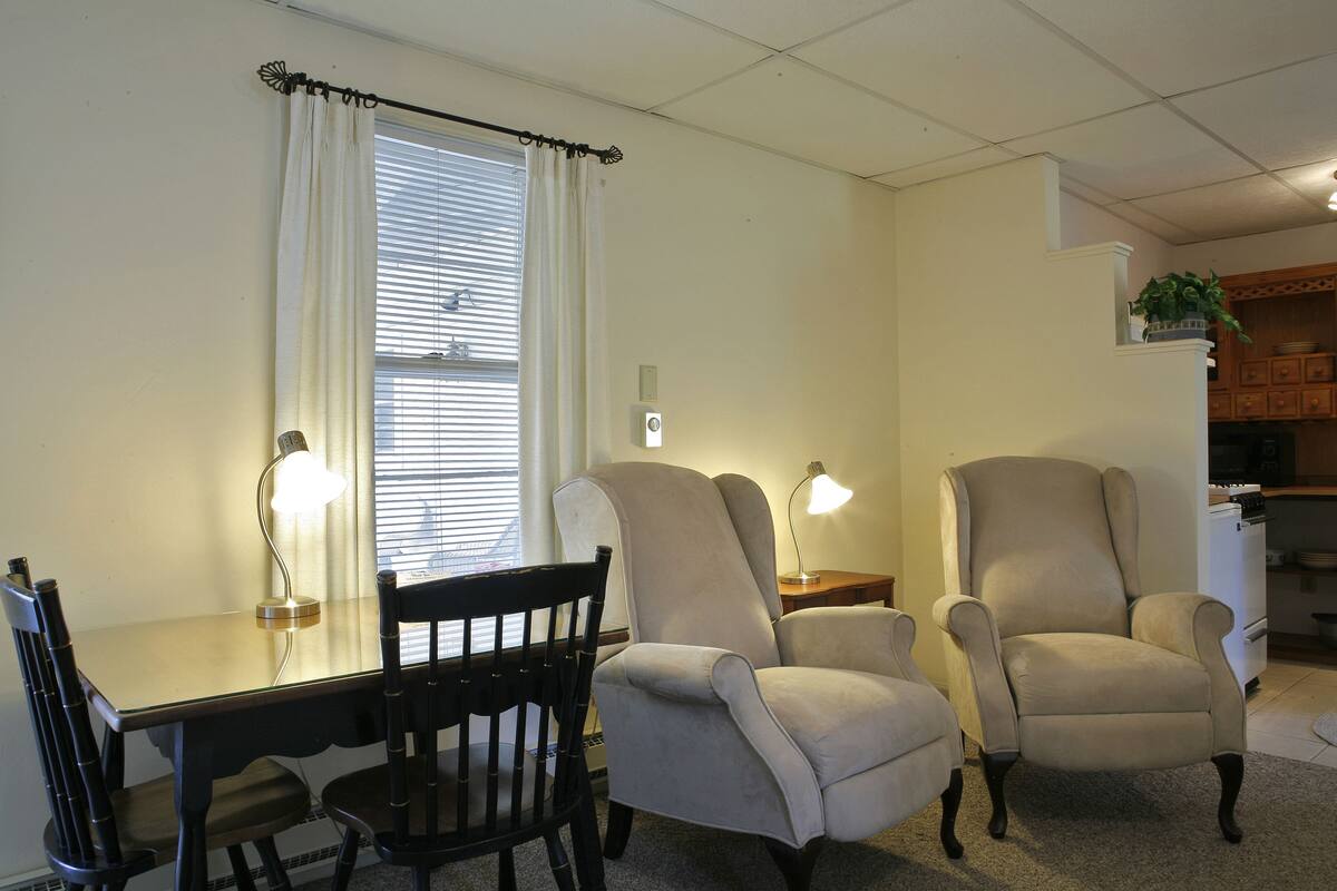 A living room with a dining table, two armchairs, a lamp, and a window with curtains.