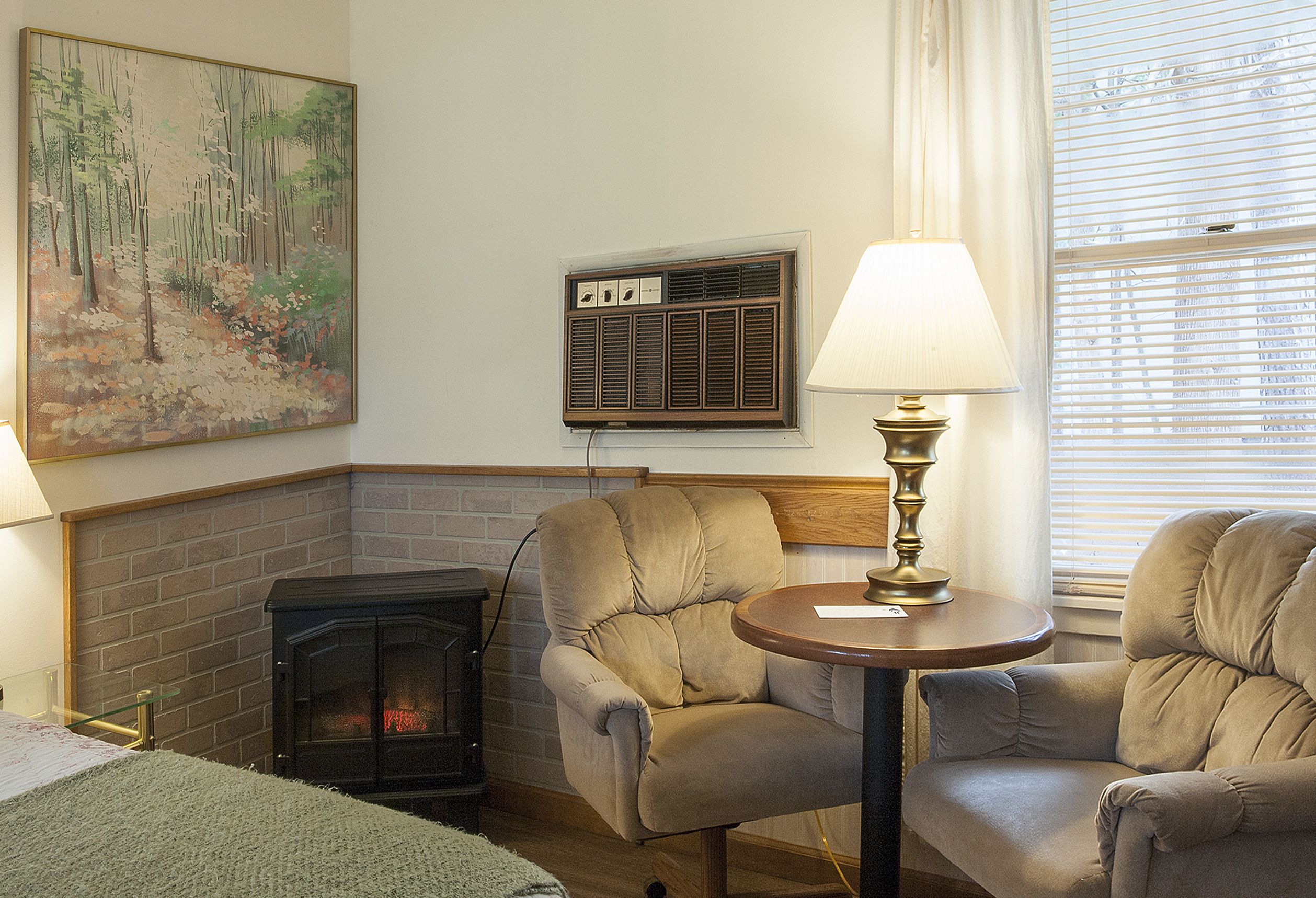 Una habitación acogedora con chimenea, dos sillones, una mesa con lámpara y un cuadro en la pared.