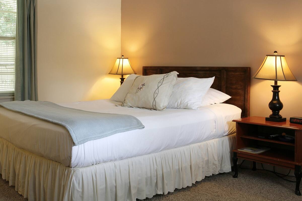 A neatly made bed with white linens, a blue throw blanket, and decorative pillows. There are two bedside lamps on wooden nightstands.