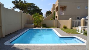 Piscina retangular com borda azulejada, cercada por um terraço de tijolos.