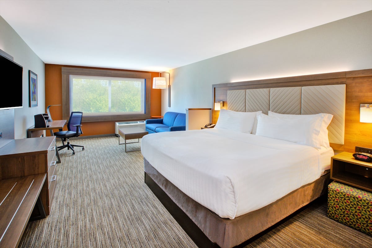 A hotel room with a large bed, a desk, a chair, a TV, and a window.