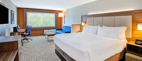 A hotel room with a large bed, a desk, a chair, a TV, and a window.