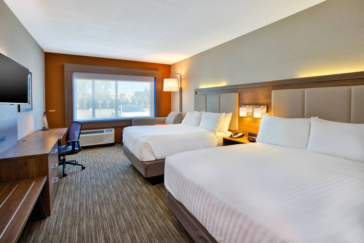 A hotel room with two beds, a desk, a chair, a TV, and a large window.