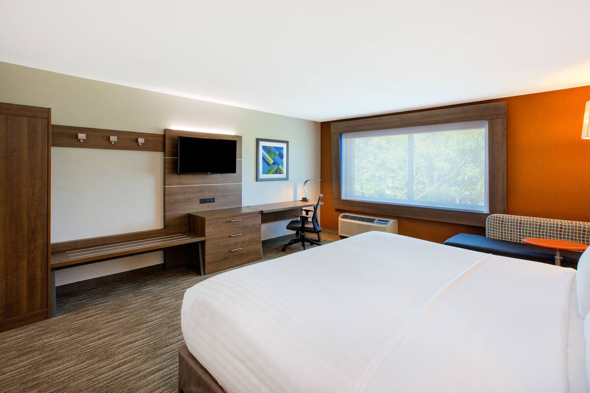 A hotel room with a bed, desk, chair, TV, and window.