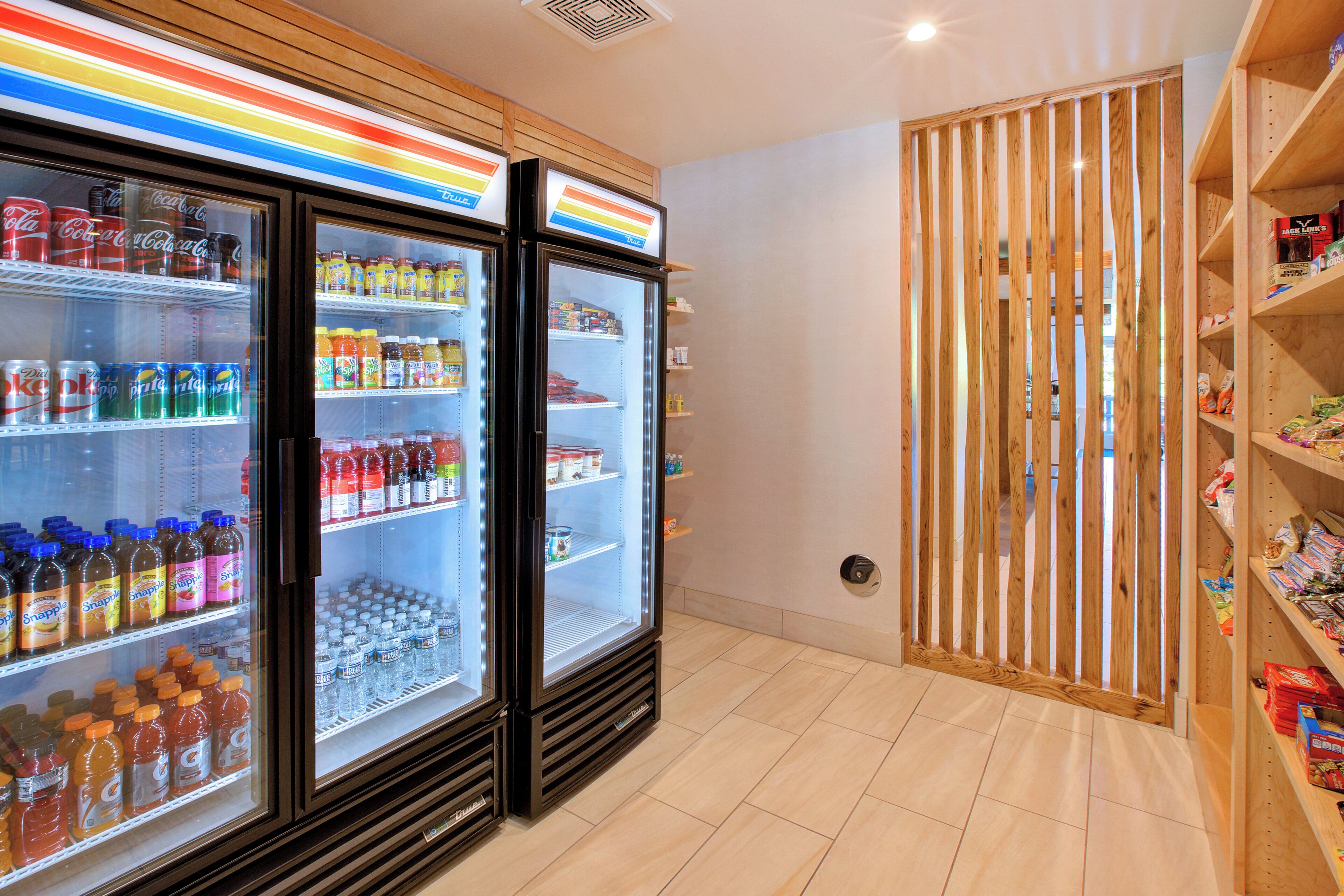 Un refrigerador exhibe diversas bebidas y una partición de madera con estantes a la derecha.