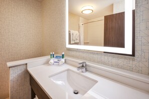 A modern bathroom with a large mirror, a white sink, and a shower area.