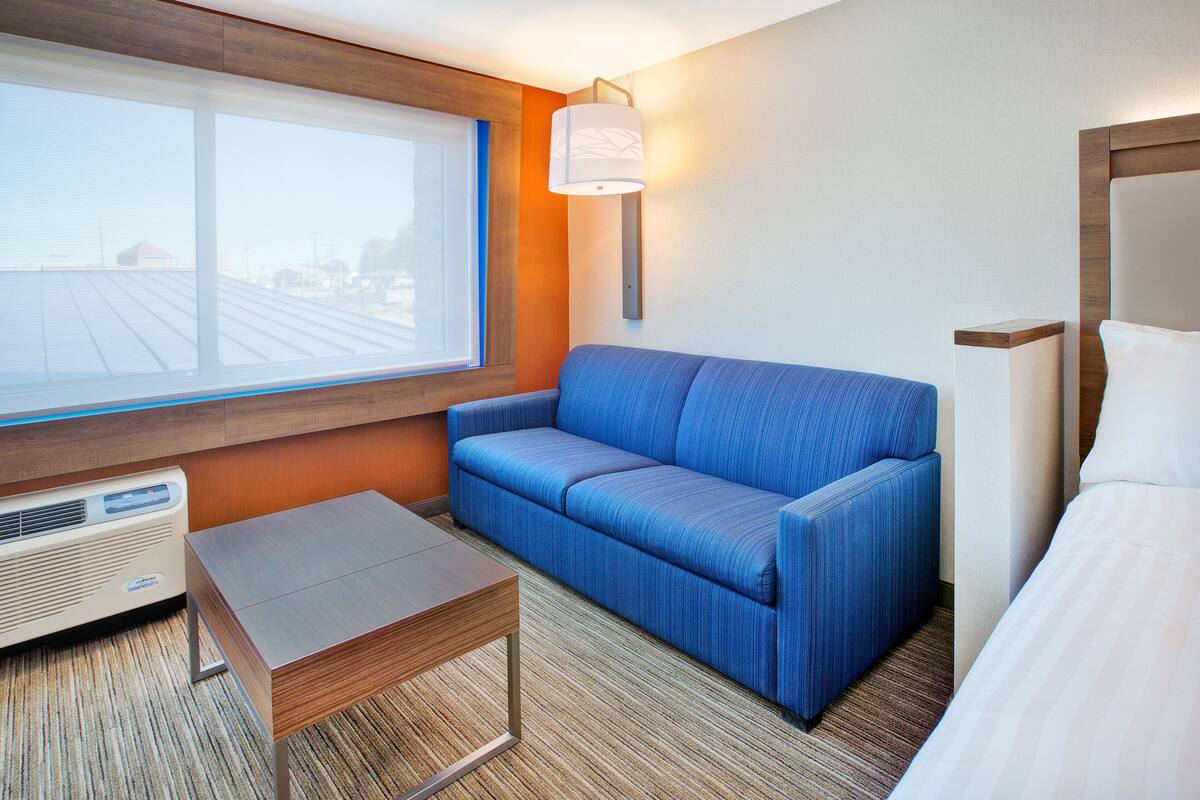 A hotel room with a large window, a blue sofa, a wooden table, and a bed.