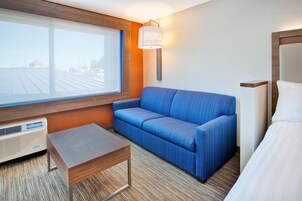 Quarto de hotel com uma janela grande, um sofá azul, uma mesa de madeira e uma cama.