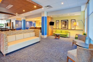 A hotel lobby with a seating area, a reception desk, and a television screen.