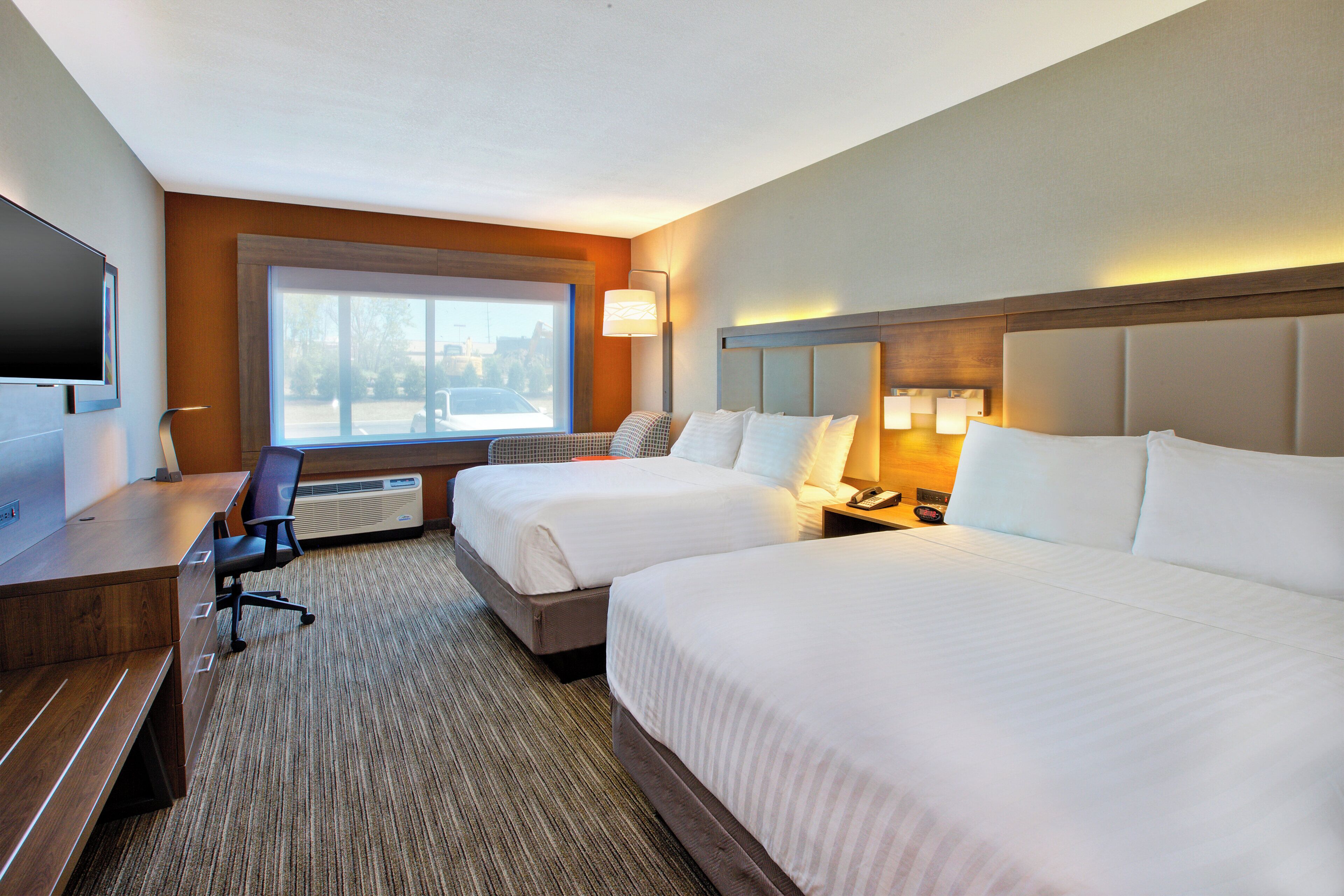 A hotel room with two beds, a desk, a chair, a TV, and a window with a view.