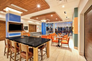 A modern interior with a black table, wooden chairs, and orange seating. - Holiday Inn Express & Suites New Castle by IHG (New Castle)