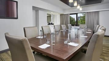 A conference room with a large wooden table, beige chairs, and a modern chandelier.