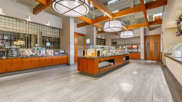 A spacious hotel lobby with a central buffet area, wooden beams, and a high ceiling.