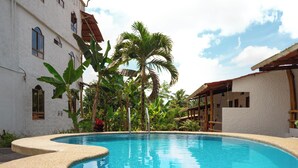 A swimming pool with a curved edge, surrounded by lush greenery and a white building with multiple windows. - Twin Hotel Galapagos (Bella Vista)
