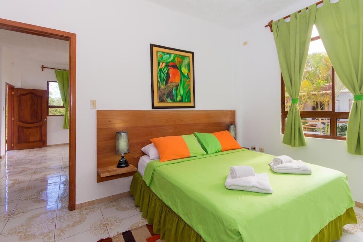 A hotel room with a bed, a nightstand, a lamp, a painting, and a window with curtains.