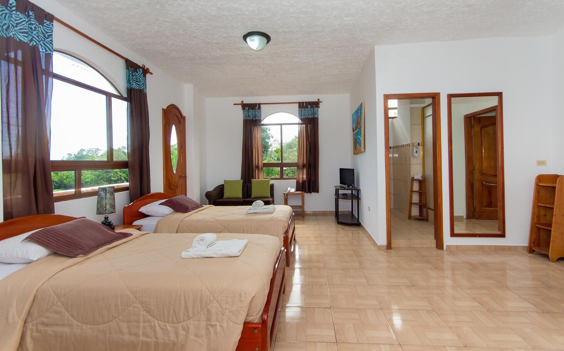 Quarto de hotel com duas camas, televisão, escrivaninha e banheiro visível por uma porta aberta.