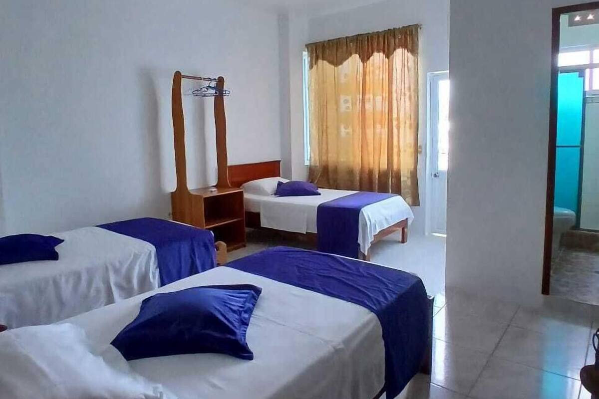 A hotel room with three single beds, a wooden dresser, a mirror, and a window with curtains.