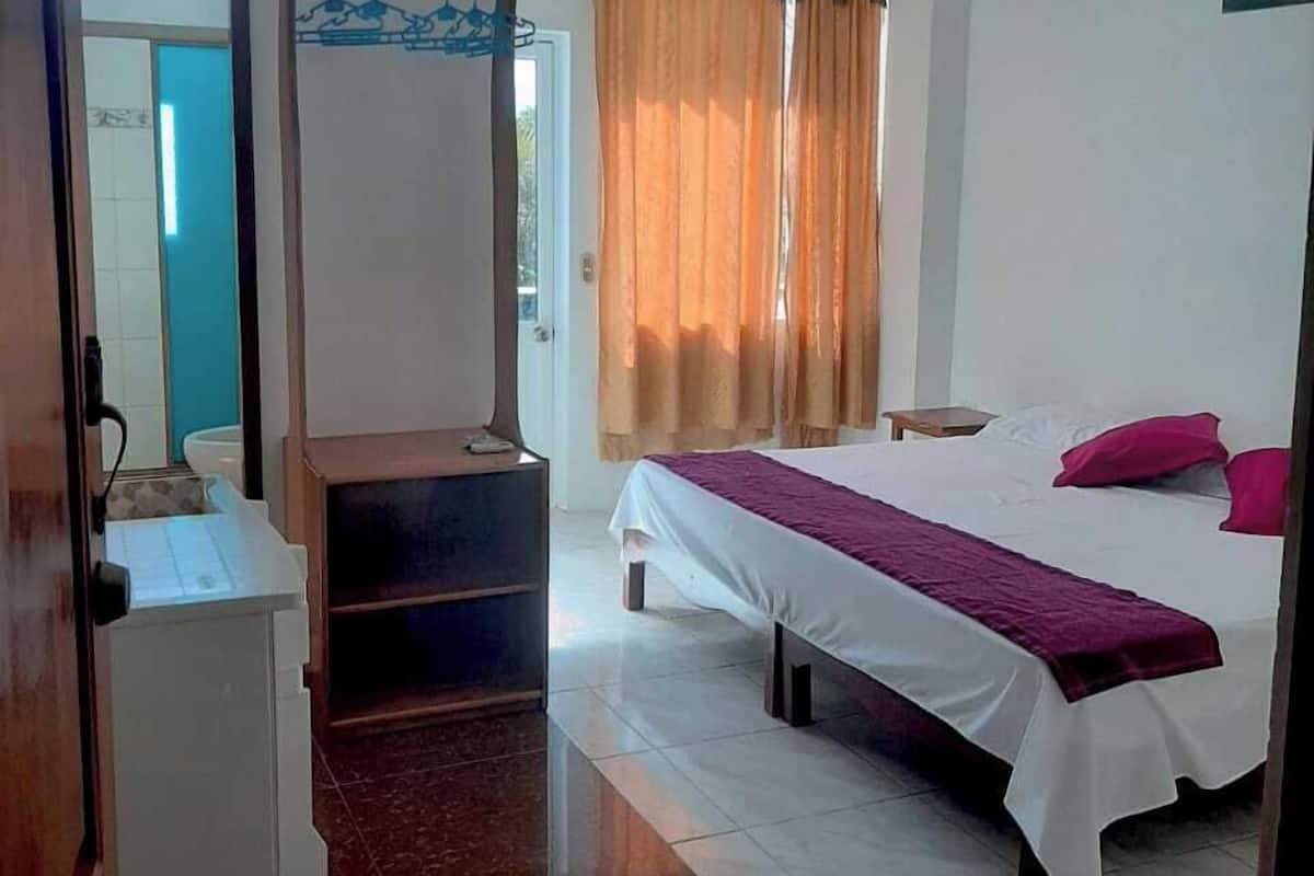 A hotel room with a bed, a desk, a mirror, and a window with curtains.
