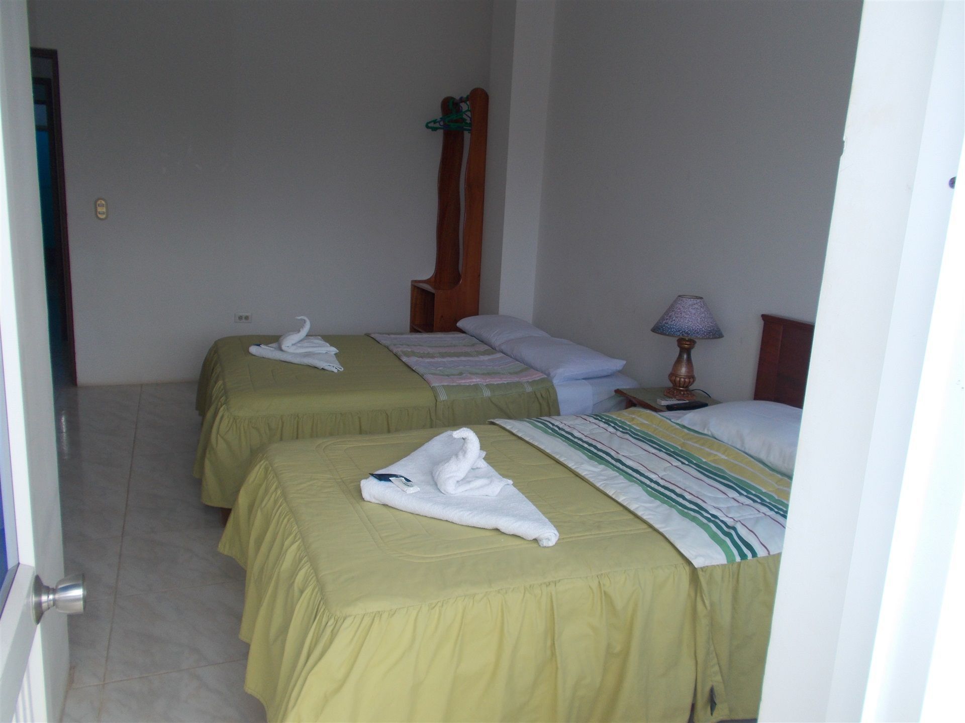 A hotel room with two single beds, each with a towel and a wooden headboard. There is a nightstand with a lamp and a book.