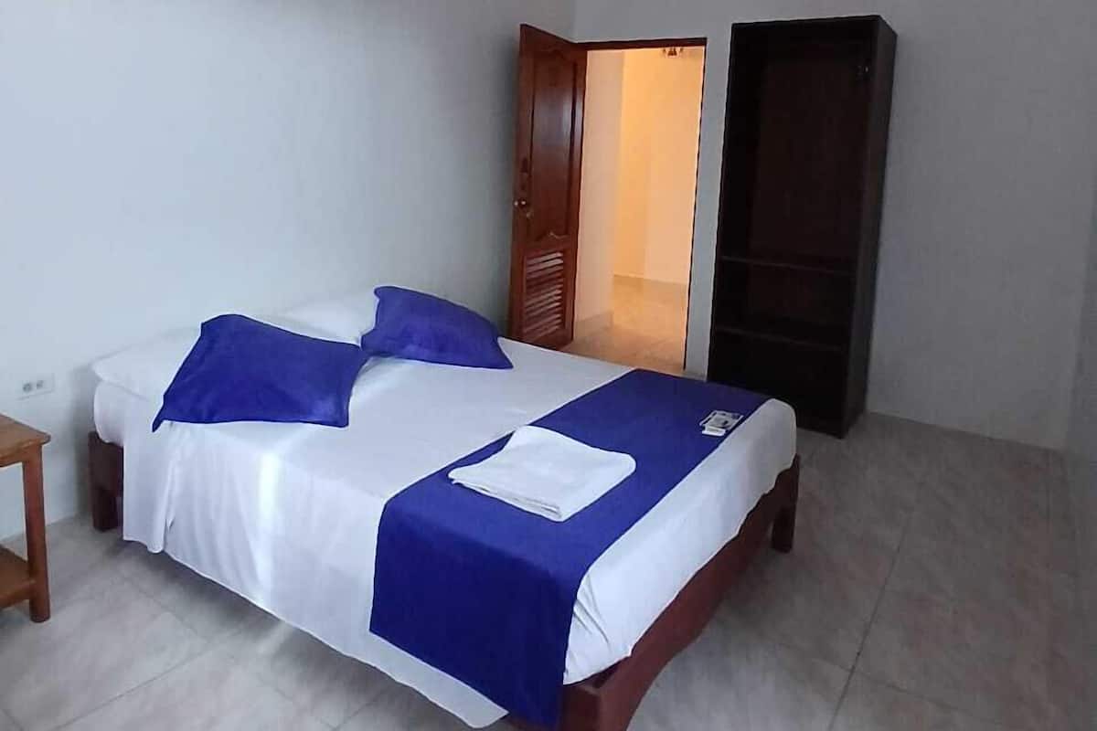 A single bed with a blue and white bedspread, a wooden nightstand, and a door leading to another room.