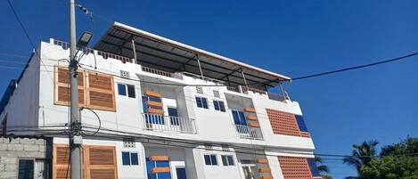 Un edificio de dos plantas con techo plano, varios balcones y una combinación de estilos de ventanas.