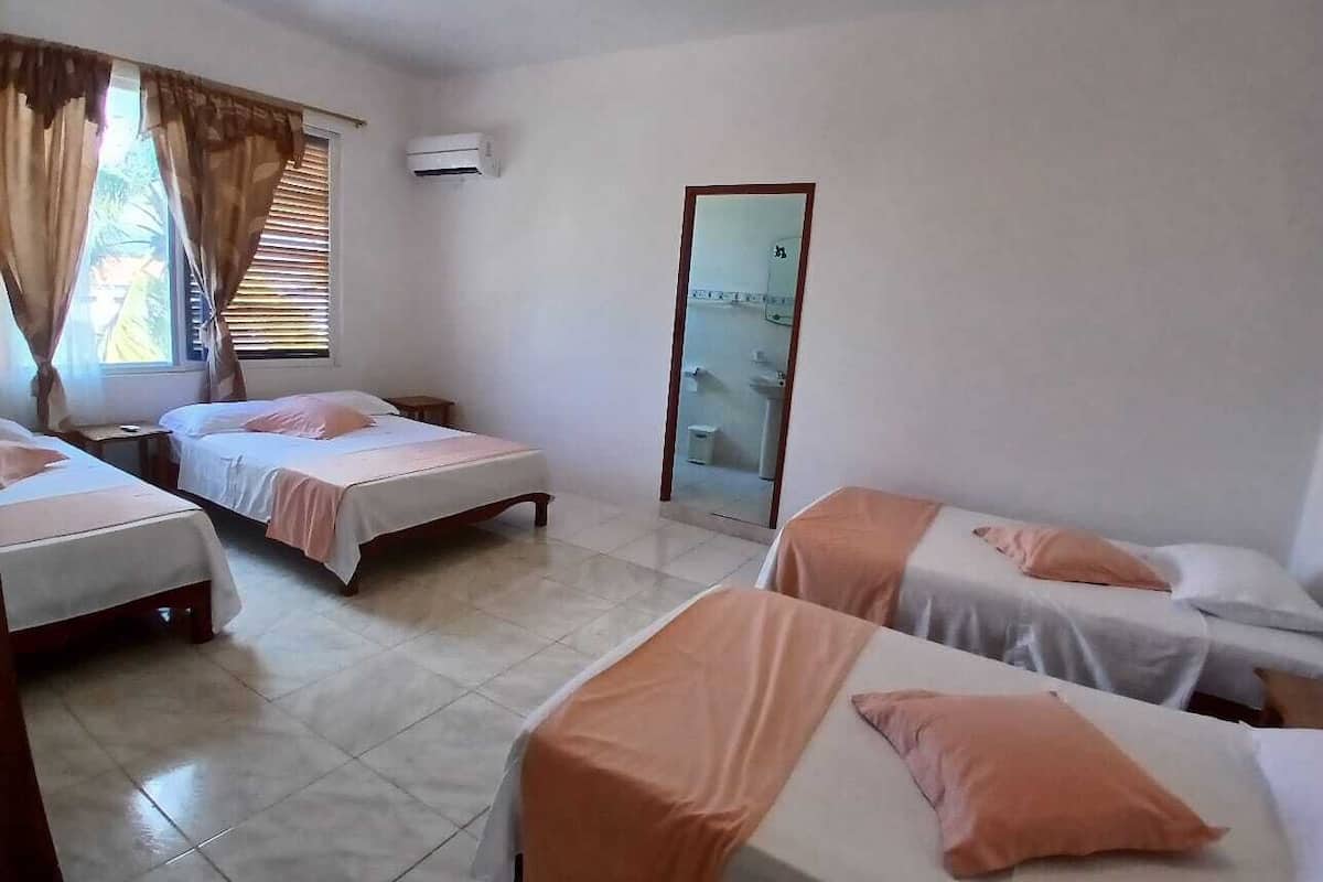 A hotel room with four single beds, a large mirror, and a window with curtains.
