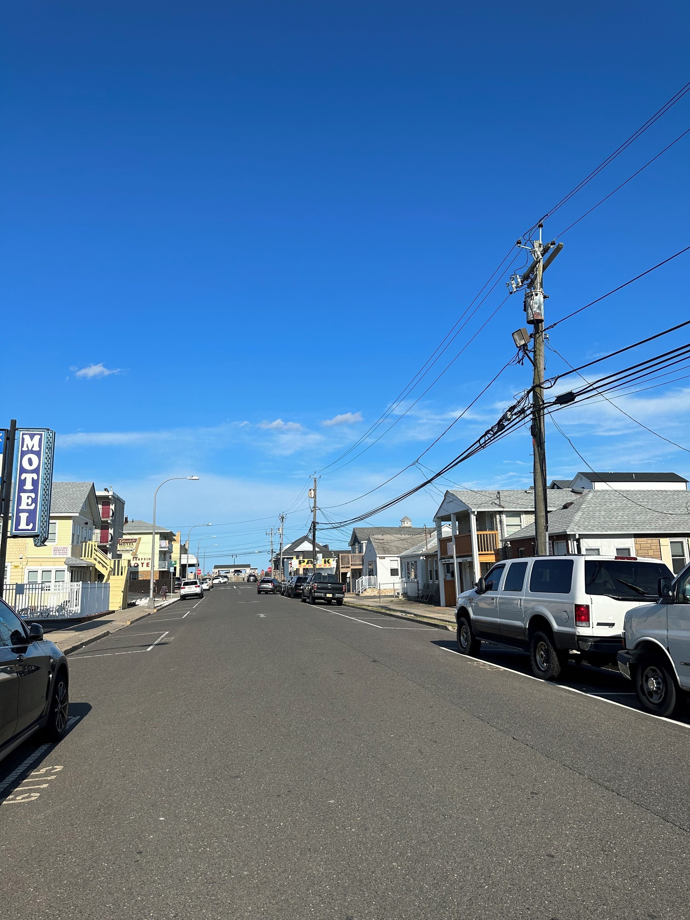 A street with a motel sign, parked cars, and utility poles.