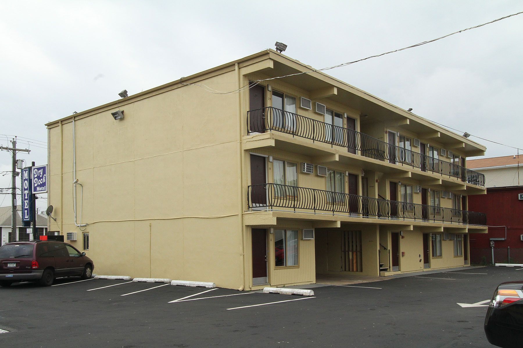 A two-story motel with a flat facade, multiple balconies, and a parking lot in front.