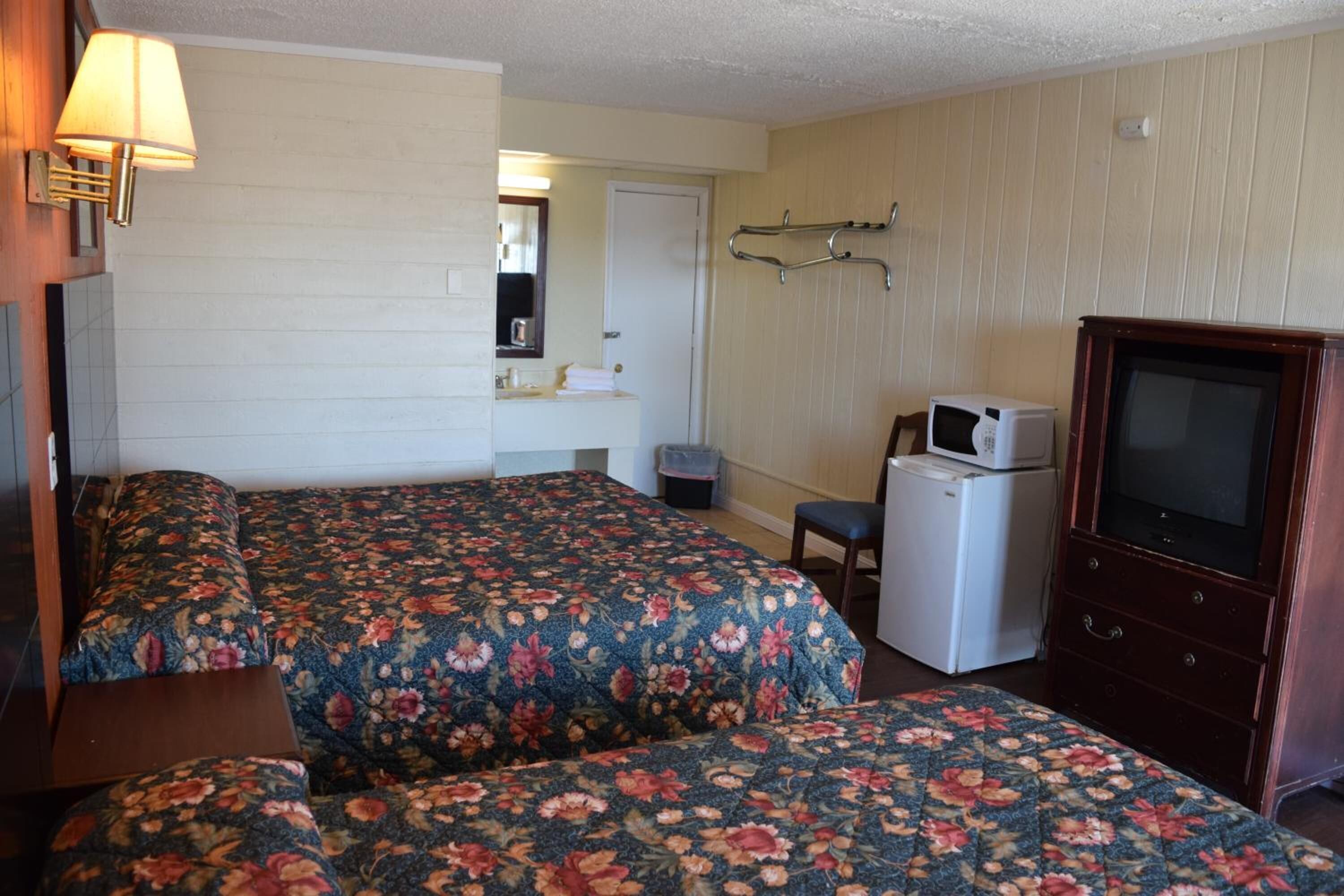 Quarto de hotel com duas camas, uma kitchenette pequena, uma televisão e um espelho.