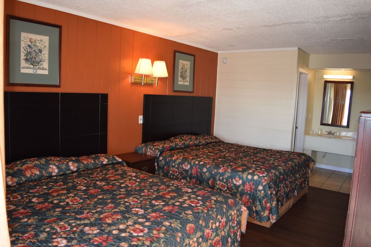 A hotel room with two beds, wooden paneling on the walls, a headboard, and a bathroom with a mirror and sink.