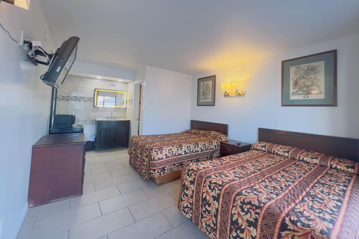 A hotel room with two beds, a desk, a mirror, and a bathroom visible through an open door.