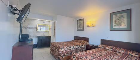 A hotel room with two beds, a desk, a mirror, and a bathroom visible through an open door.