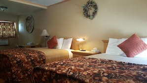 A hotel room with two beds, a desk, a lamp, a wall clock, and a decorative wreath. - Trails End Motel (Lewistown)