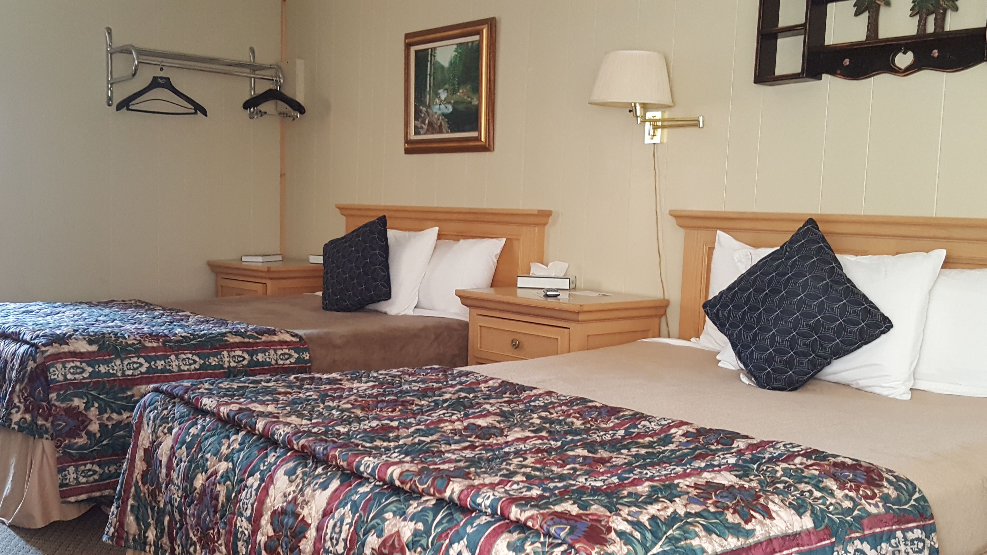 Une chambre d’hôtel avec deux lits, une table de chevet avec une lampe, un tableau au mur et un porte-manteau.