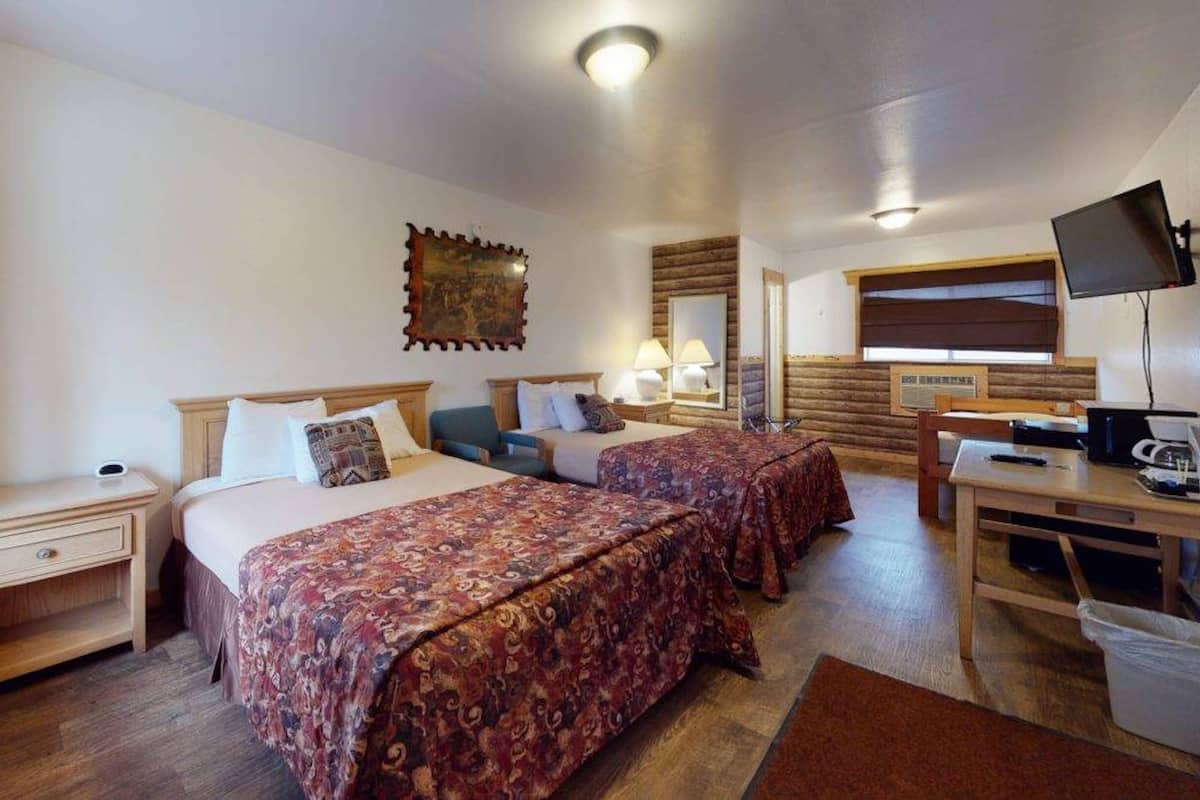 A hotel room with two beds, a desk, a chair, a TV, and a window with blinds.