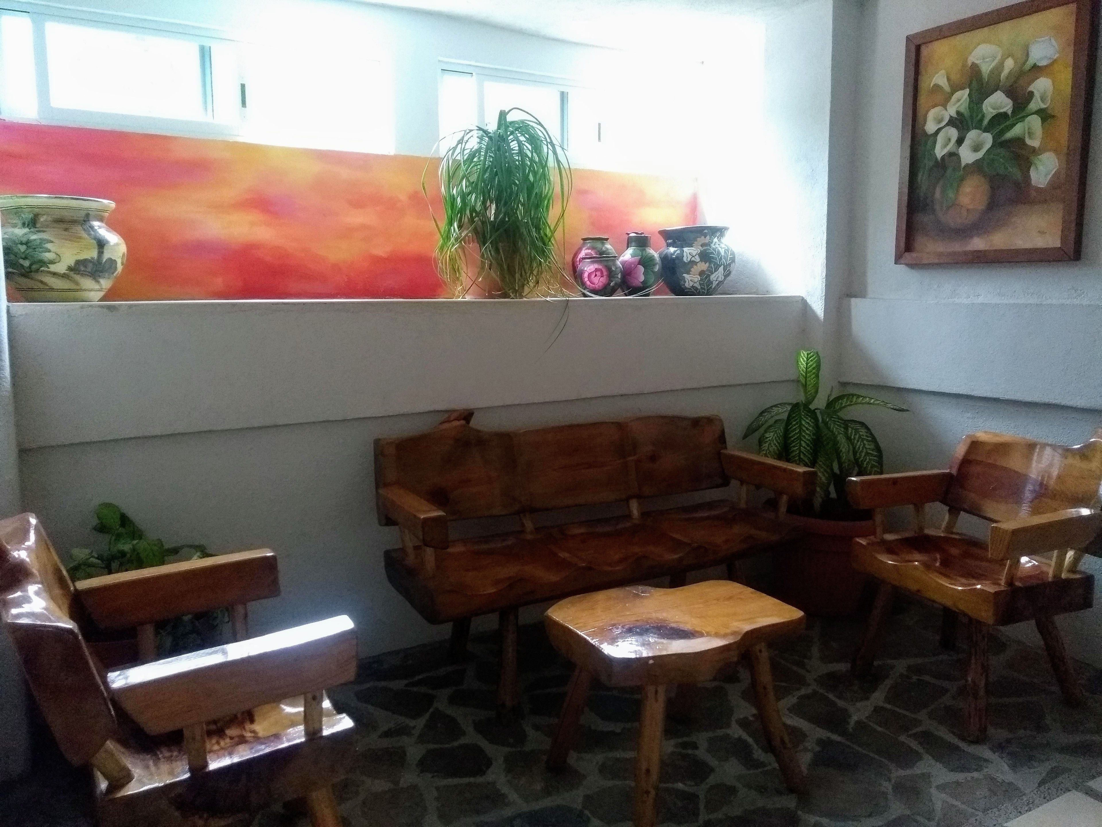 Una habitación con un sofá de madera, dos sillas de madera, una mesita pequeña y una planta en maceta.